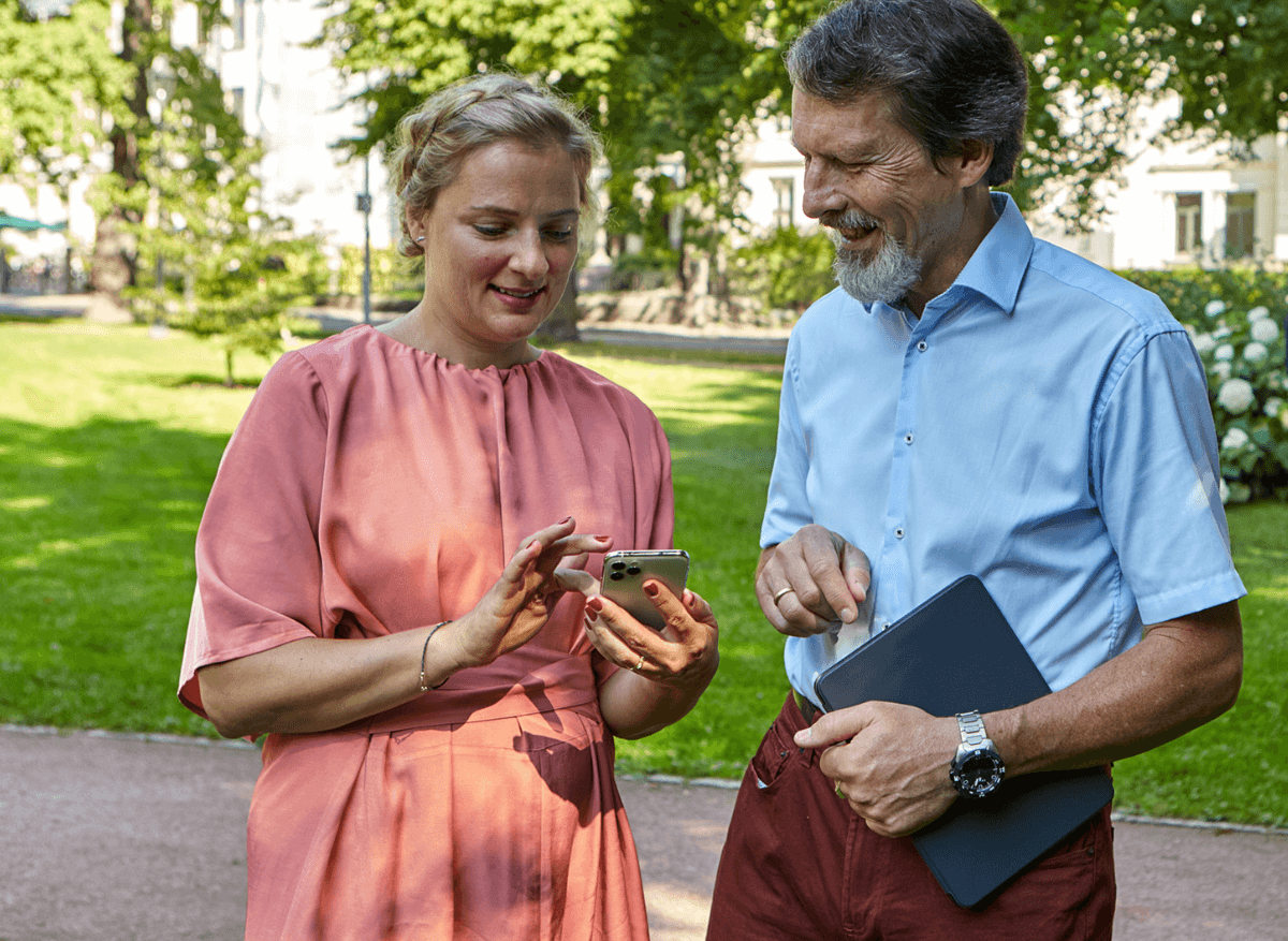 Two colleagues outside in a green park, looking at a mobile 